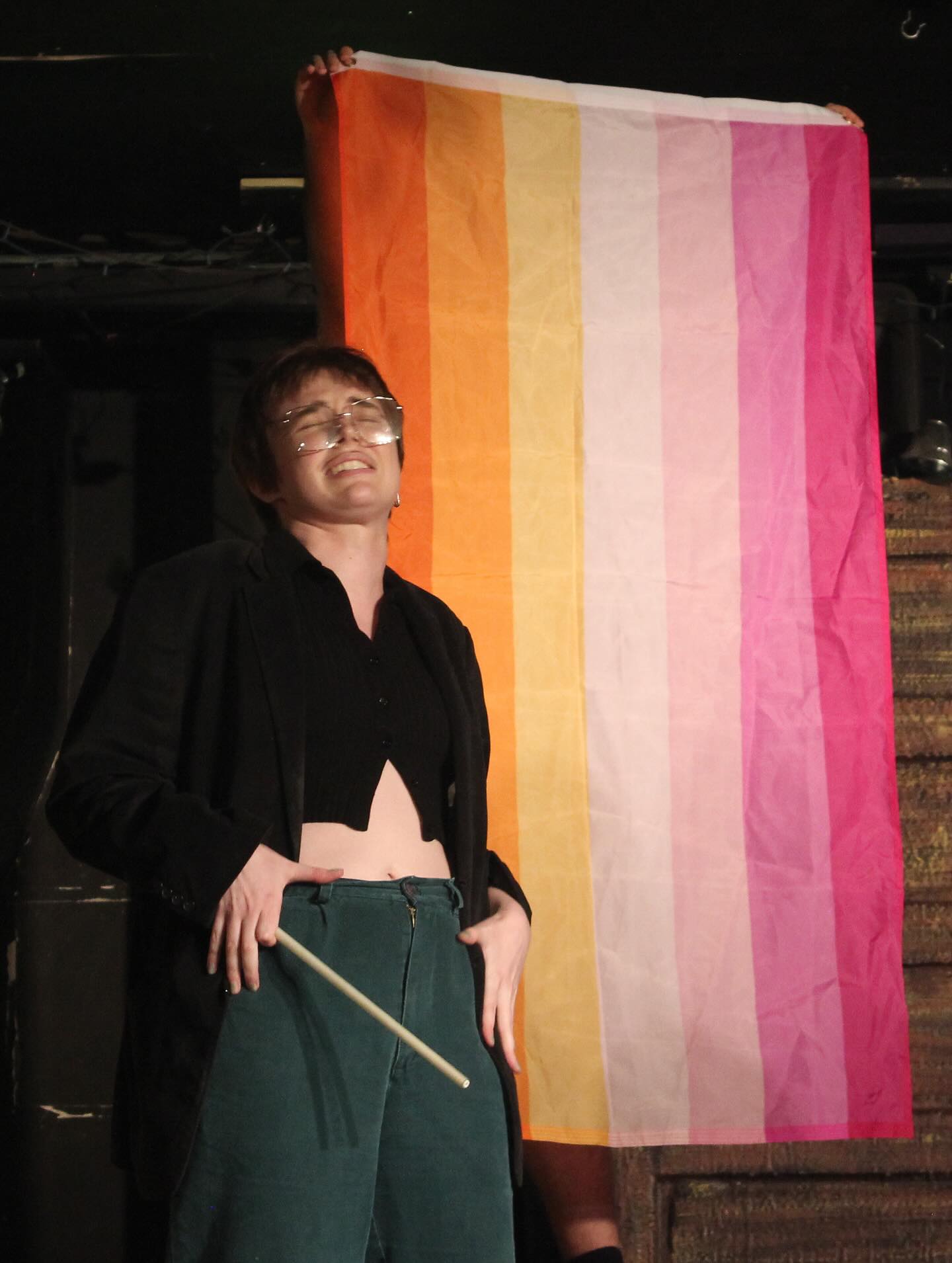 a man smiles and touches his hips in front of the lesbian flag